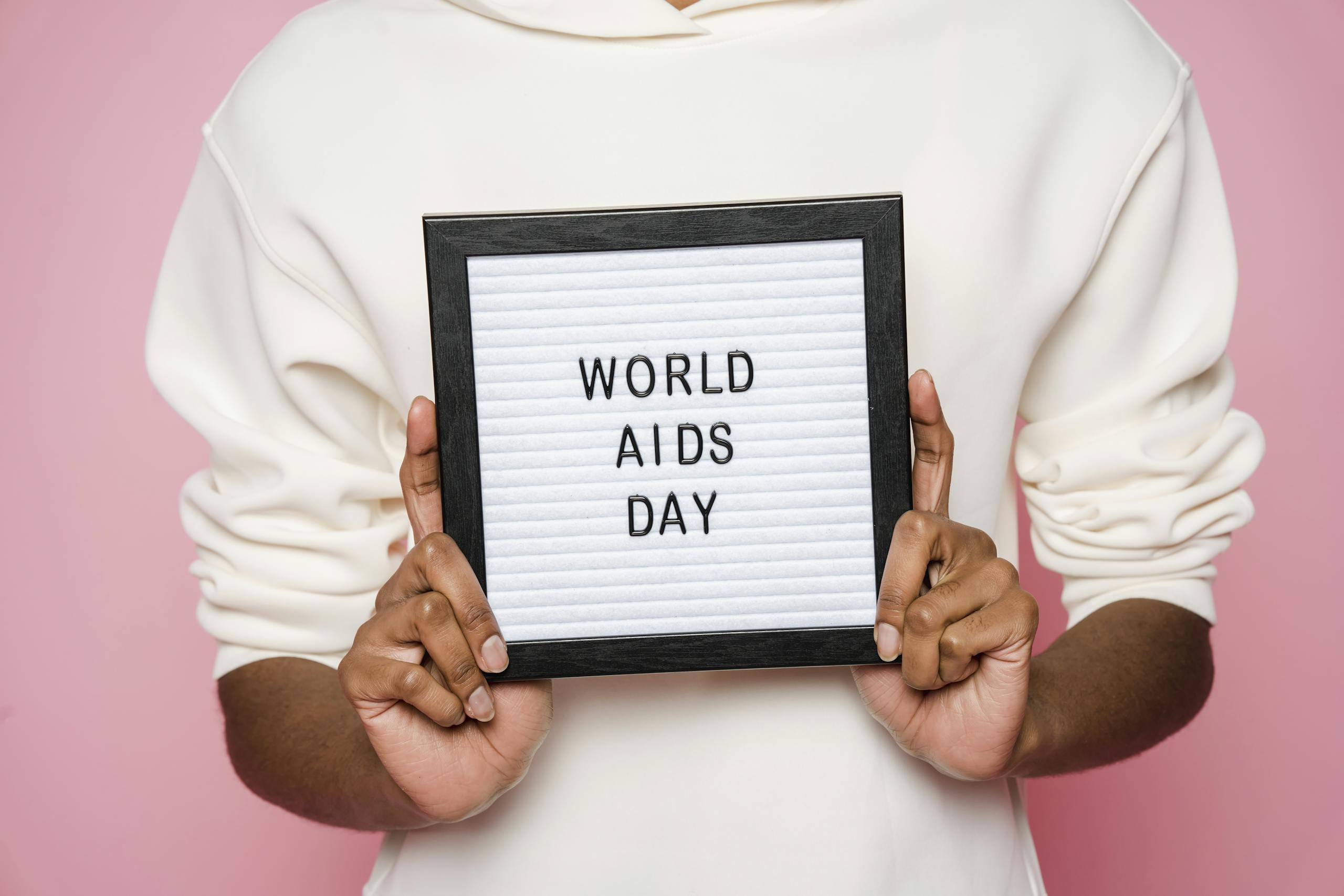 A person holding a sign with World AIDS Day message on pink background.