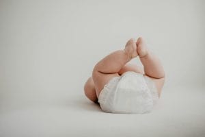 Cute baby lying on back in a diaper against a soft, white background.