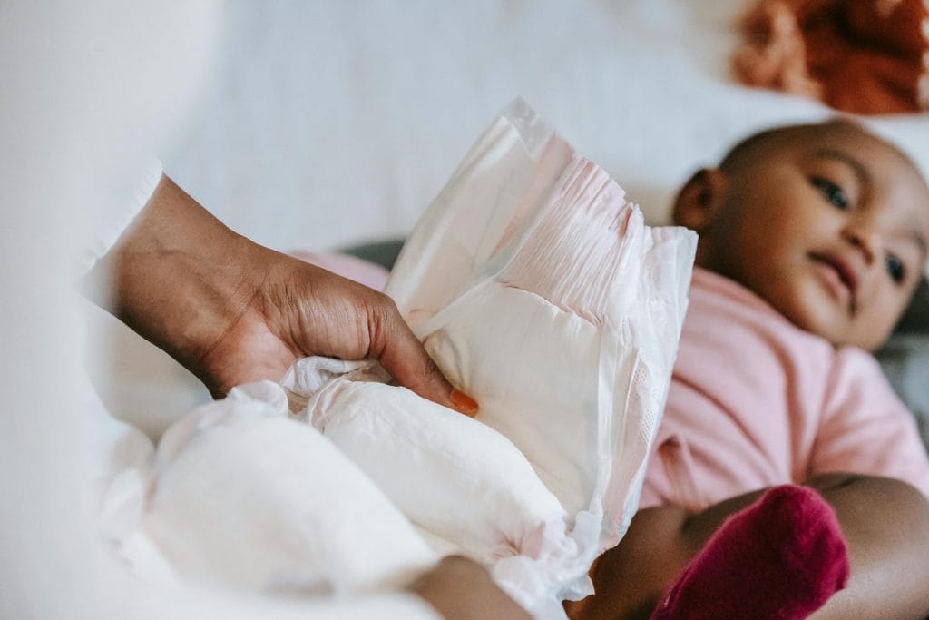 A mother gently changes her baby's diaper in a calm, cozy home setting.